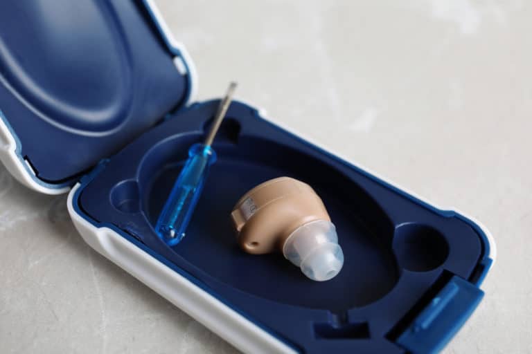 An ITE hearing aid in a repair workspace next to a tiny screwdriver