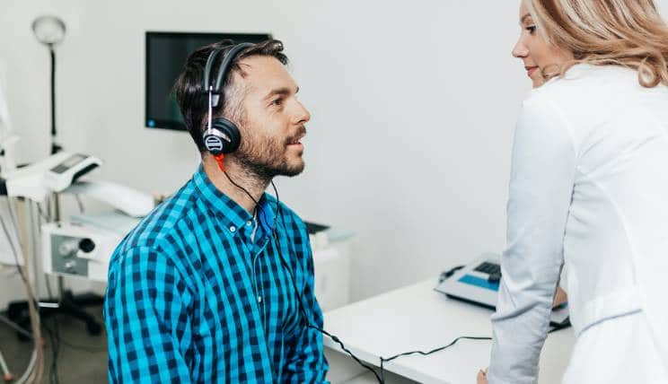 An adult wearing headphones for a hearing test which the audiologist is setting up
