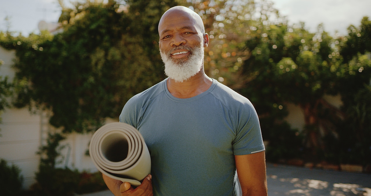 An older man holding a rolled-up yoga mat