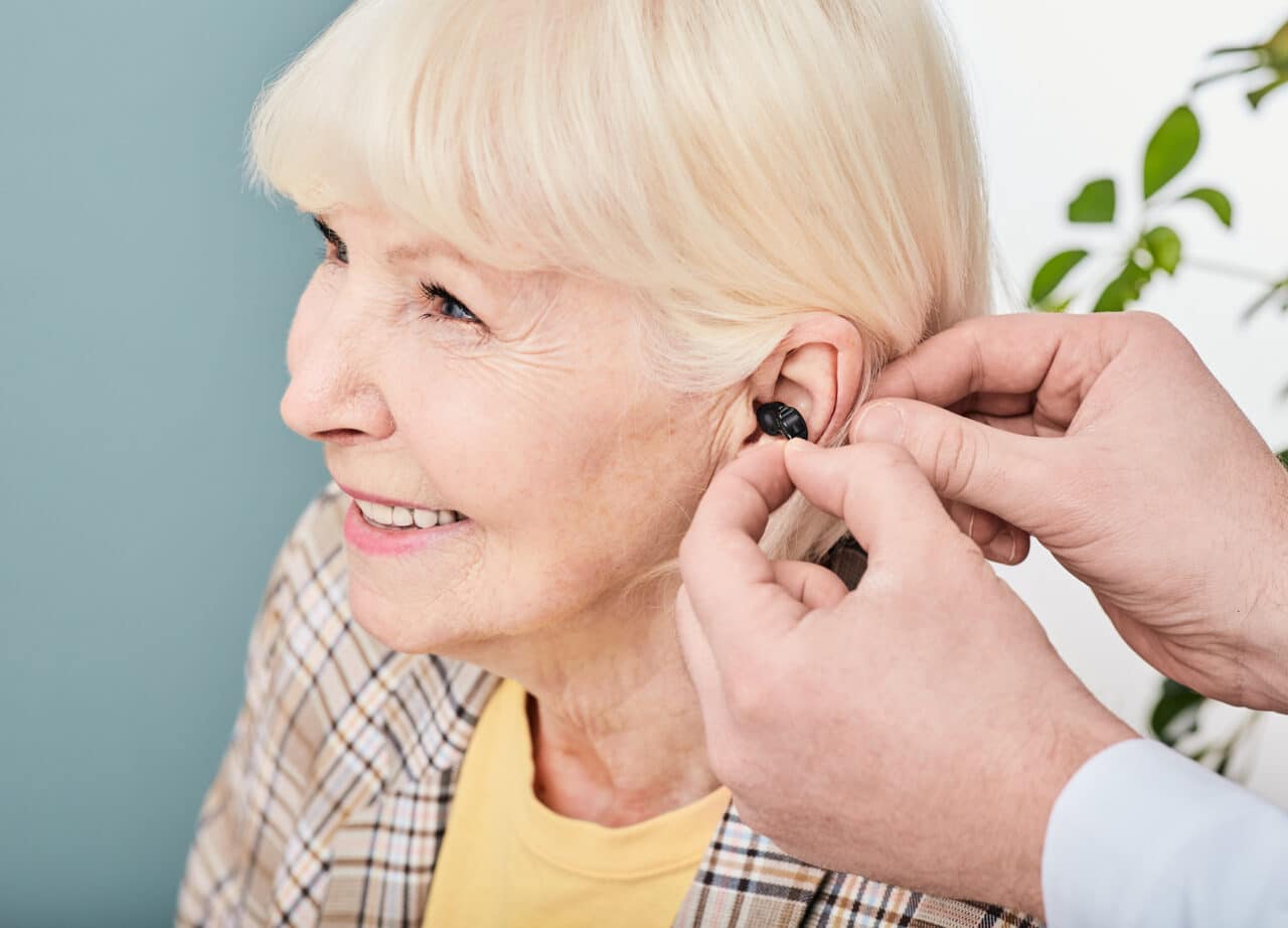 Audiologist inserting hearing aid into the ear of a senior woman patient.