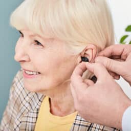 Audiologist inserting hearing aid into the ear of a senior woman patient.