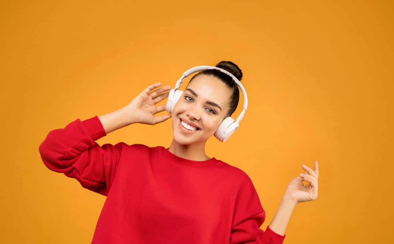 Woman wearing over-the-ear headphones in front of an orange background.