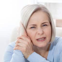 Woman with tinnitus holding her ear looking annoyed