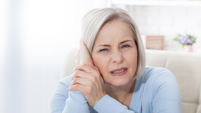 Woman with tinnitus holding her ear looking annoyed.