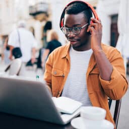 A man does a hearing screening online, wearing headphones at an outdoor cafe.