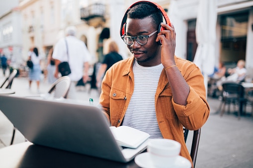 A man does a hearing screening online, wearing headphones at an outdoor cafe.