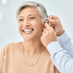 A woman smiles as her audiologist puts her new hearing aids on her ears.