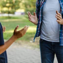 Two men discussing something at the park, you can only see their bodies, their hands are spread out as though an issue has ocurred.
